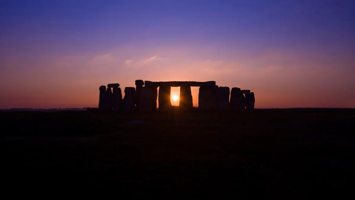 Stonehenge in controluce, con il sole tra le pietre sotto un cielo viola e arancione: geometria sacra e numeri del cielo